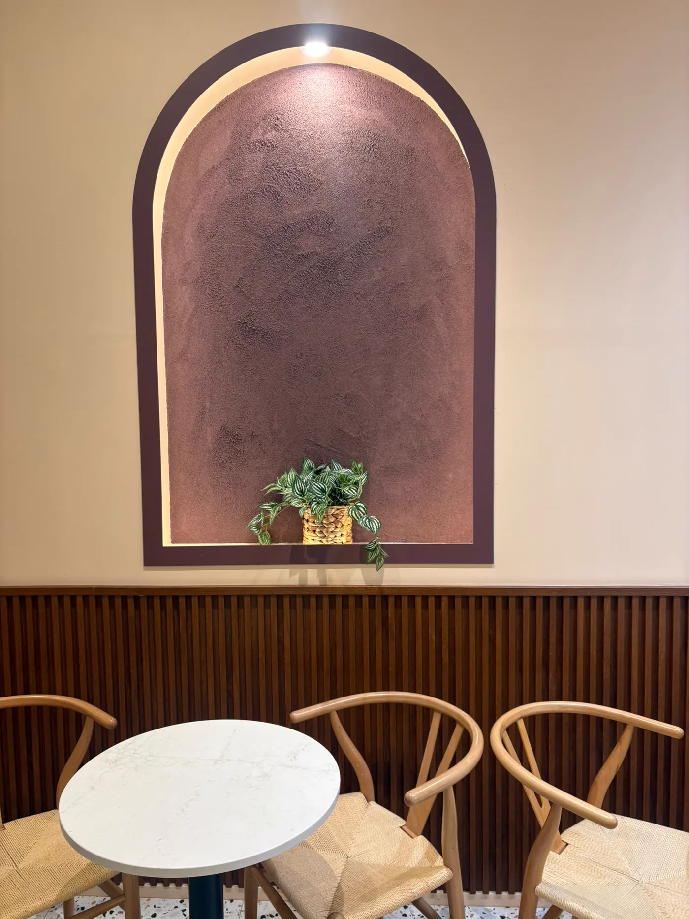 The arched, lit alcove and timber panelling inside Nabil's Açaí Station in Mount Lawley, with a marble table and wishbone chairs