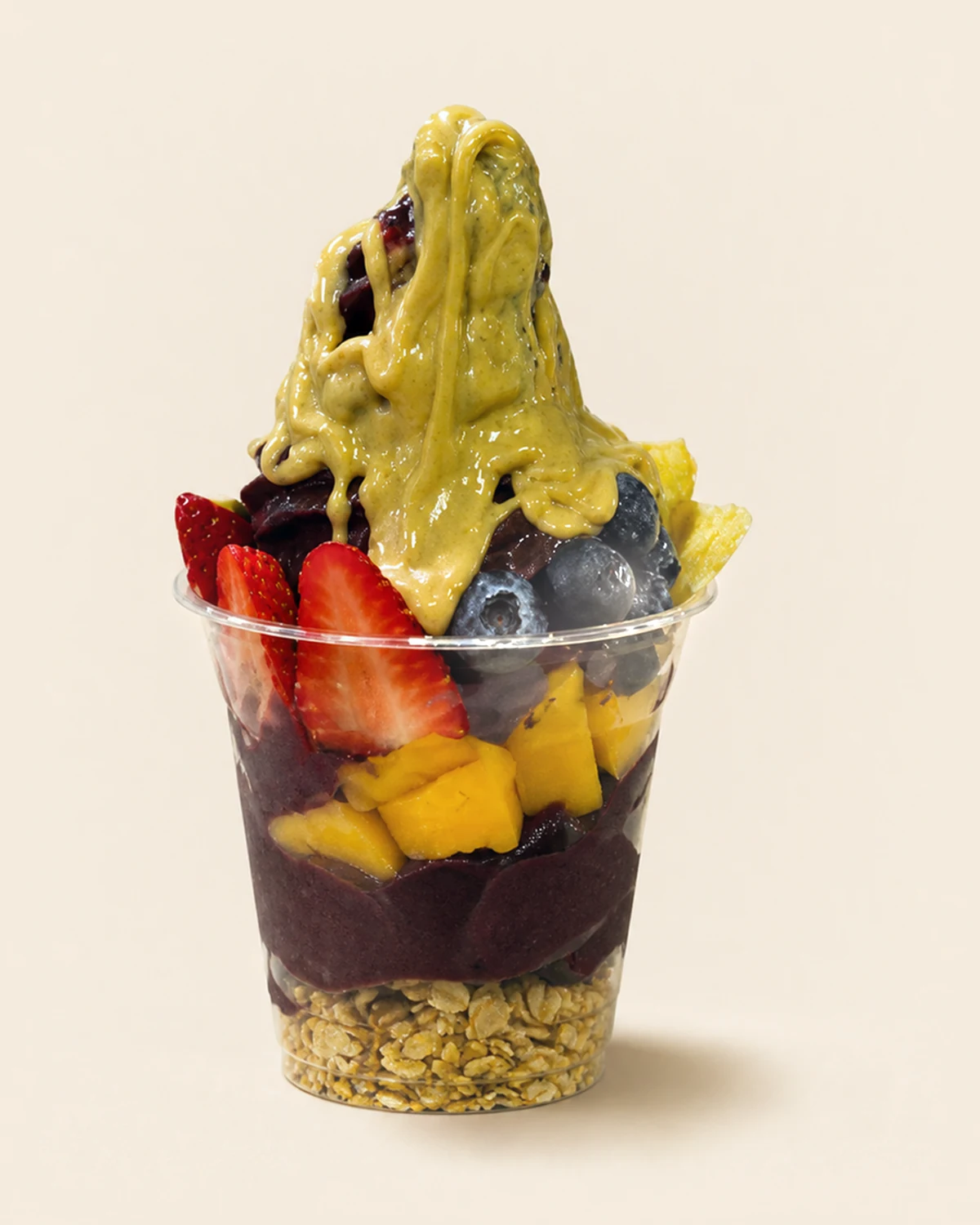A clear cup of Nabil's açaí layered over granola with mango, blueberries and strawberries, under a thick pale green drizzle